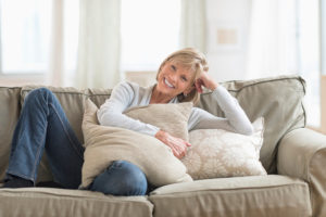 A woman smiles as she lies on a couch. She holds onto a pillow and appears comfortable.