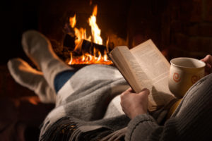 A person reads a book near a fireplace.