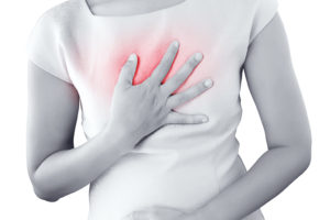 A woman is experiencing heartburn and holds onto her chest.