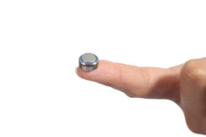 A button battery lies on someone's finger.