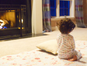 A young kid sits near a fireplace.