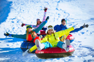 A group of kids sled down a hill full of snow. They all appear happy.