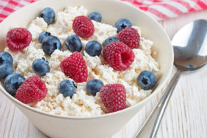 A bowl of cottage cheese is in focus. Blueberries and raspberries are on top of the cottage cheese.