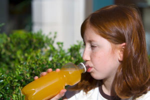 A young girl drinks an orange-colored beverage out of a bottle.