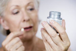 An elderly woman observes her prescription bottle as she takes one pill.