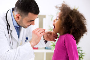 A young girl opens her mouth wide as a doctor looks in her mouth.