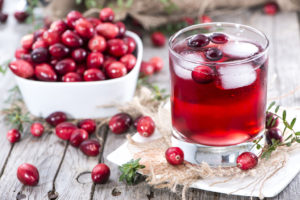 A glass of cranberries juice sits on a napkin next to a bowl full of cranberries.