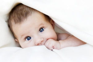 A baby with bright blue eyes plays with a white blanket.