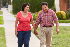 A woman and man hold hands as they walk on a sidewalk path.