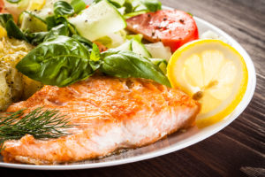 A white plate is filled with a salad and a piece of salmon.