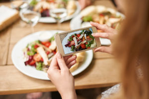 A woman uses her phone to take a picture of her meal. She appears to be eating a salad.