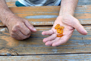 A person holds five Vitamin E pills in his hand.