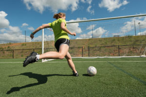 A girl kicks a soccer ball into the soccer goal.