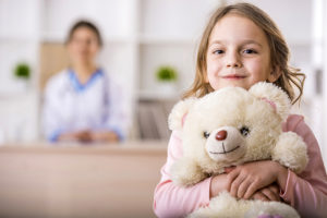 A young girl holds a white teddy bear close to her chest and smiles gleefully.