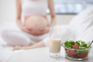 A pregnant woman sits down and stares at a salad and a glass of milk.