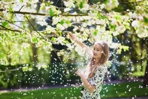 A little girl shakes a tree with white flowers. Pollen floats through the air.