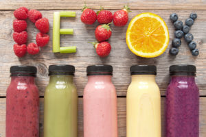 Five different smoothies are in focus. Above the smoothies are fruit placed to spell out, 'DETOX.'