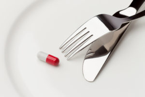 A plate holds a knife, fork and a red-and-white pill.
