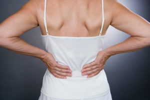 A woman places her hands on her back. She appears to have low-back pain.