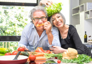 Two elderly adults play with vegetables in their kitchen.