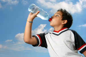 A young boy drinks water from a plastic water bottle.