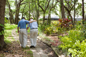 A man assists an elderly adult walk outside.