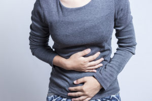 A woman holds her stomach and appears uncomfortable.