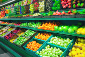 A produce aisle in a grocery store is in focus. Colorful fruits and vegetables are shown.