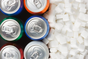 A bunch of sugar cubes are placed next to six pop cans.