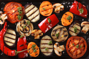 A grill holds fresh fruits and vegetables. The vegetables look sauteed.