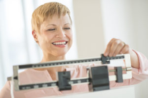 A woman adjusts her manual weight scale and smiles.