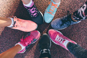 A group of people huddle together and place one foot into a circle. All of their shoes are colorful tennis shoes.