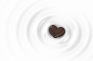 A heart-shaped piece of chocolate is surrounded by white ripples.