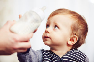 A baby boy grabs a bottle of breast milk.