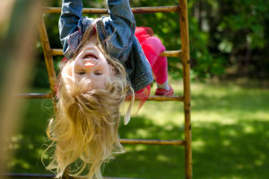 A young girl hangs upside down on the monkey bars.
