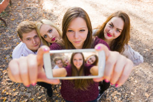 A woman holds their phone to take a selfie with three of her friends.