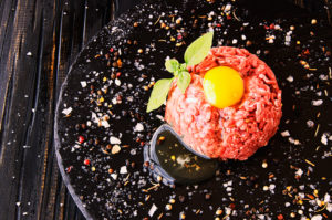 An egg yolk sits on top of a ground beef patty.