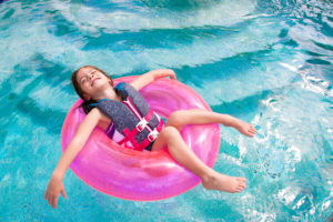 A young girl wears a life jacket and lies in a pink round pool float.