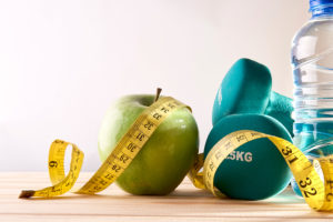 Measuring tape surrounds an apple, dumbbells and a water bottle.