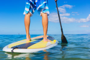 A man stands on a paddleboard in the middle of the ocean.