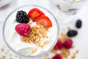 A bowl of yogurt is shown with a little bit of granola and berries on top.