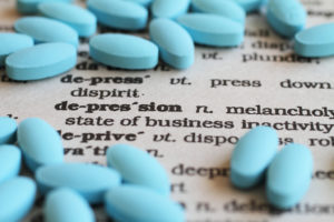 A few blue pills are shown on top of a dictionary. The word, depression, is in focus.