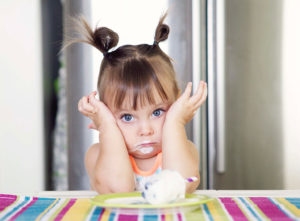 A young girl rests her face in her hands and appears uncomfortable. A plate of ice cream is in front of her.