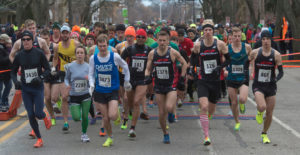 A group of runners participate in a race. They all wear work out clothes and colorful tennis shoes.
