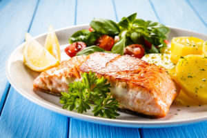 A piece of fish is on a white plate with a salad and lemons.