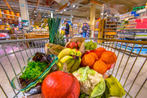 A grocery cart is filled with fresh produce and whole foods, such as oranges, bananas, apples and more.