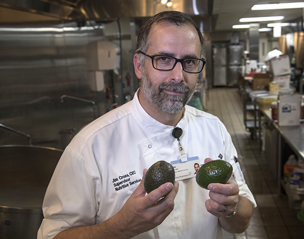 Chef Jim Cross holds an avocado in each hand and smiles.