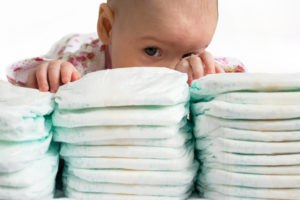 A baby places their hands on top of a pile of diapers.