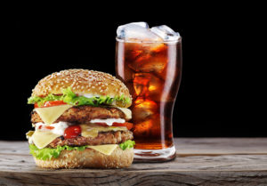 A burger is shown next to a glass full of soda.