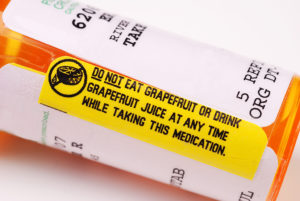 A prescription bottle is shown with a yellow sticker that reads, "DO NOT EAT GRAPEFRUIT OR DRINK GRAPEFRUIT JUICE AT ANY TIME WHILE TAKING THIS MEDICATION."